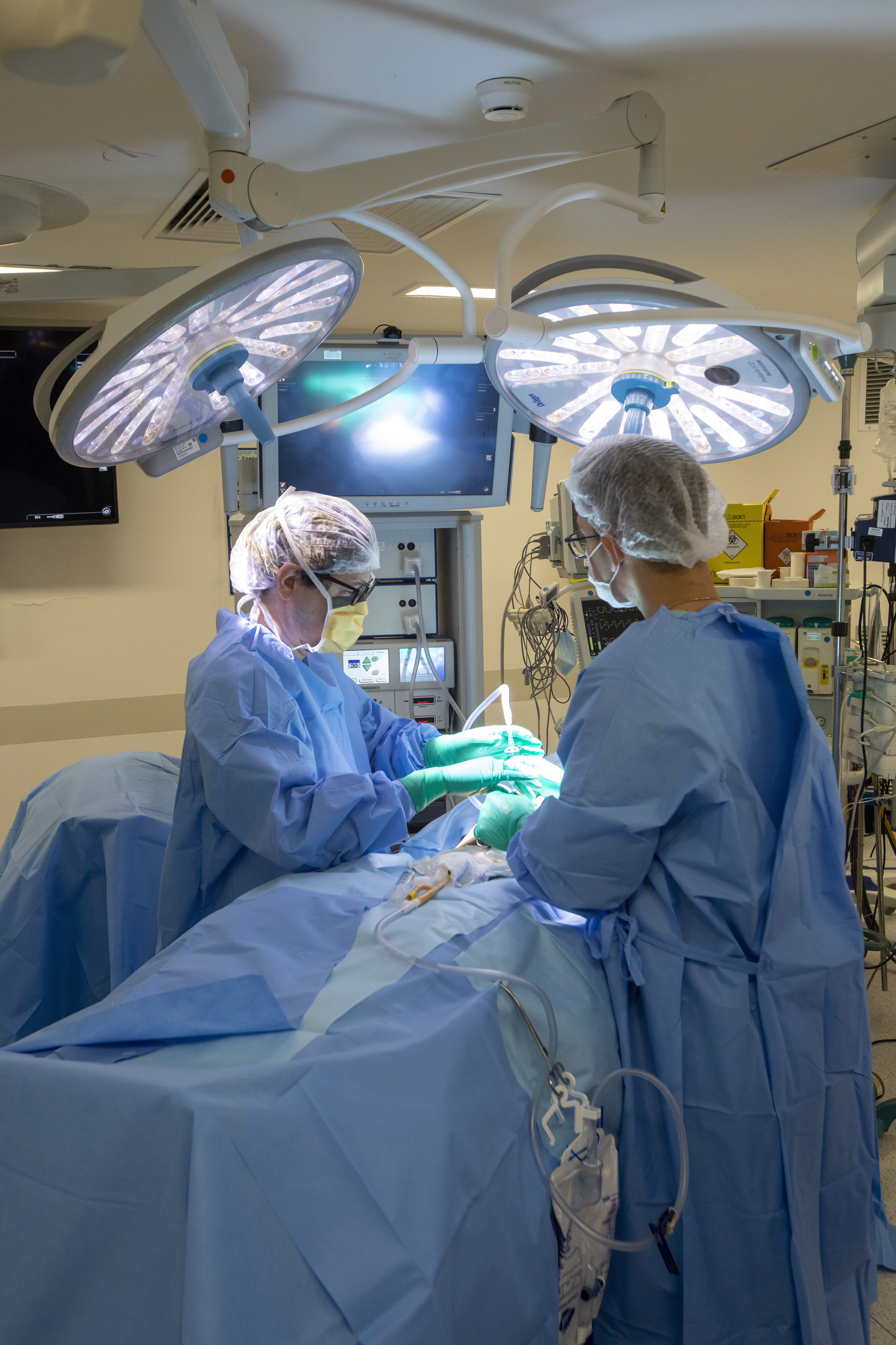 Foto mostra médicos em um centro cirúrgico com muitos equipamentos realizando uma cirurgia com o auxílio de imagens por vídeo